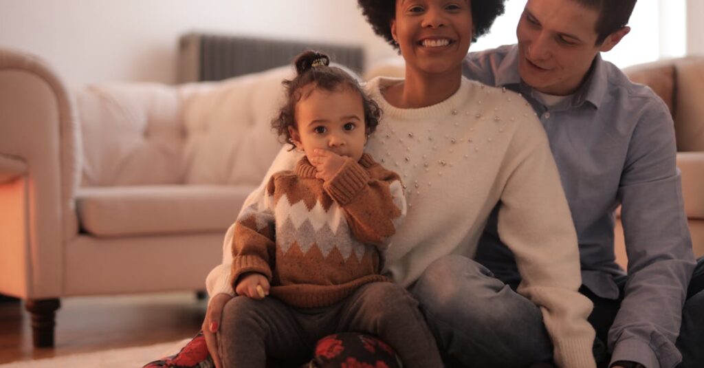 A joyful family with parents and baby enjoying time together indoors on the couch.